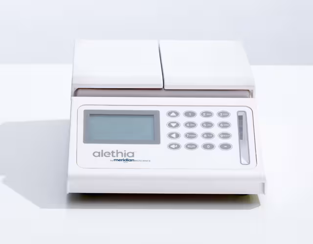 White compact electronic device with a keypad, small display, and two paper trays on top, resting on a desk