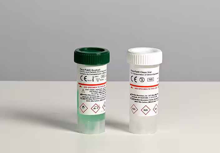 Two lab specimen containers with green and white caps on a white surface, each bearing warning labels and hazard symbols.