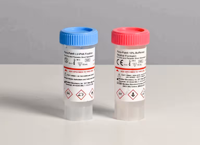 Two small specimen vials with blue and red caps sit on a lab bench, labels showing hazard pictograms and care instructions.