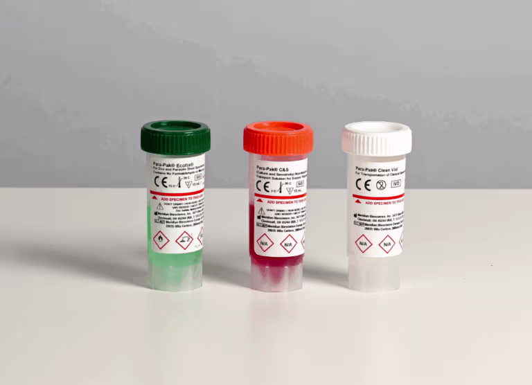 Three small lab specimen vials with green, red, and clear liquids and hazard labels on a white tabletop.