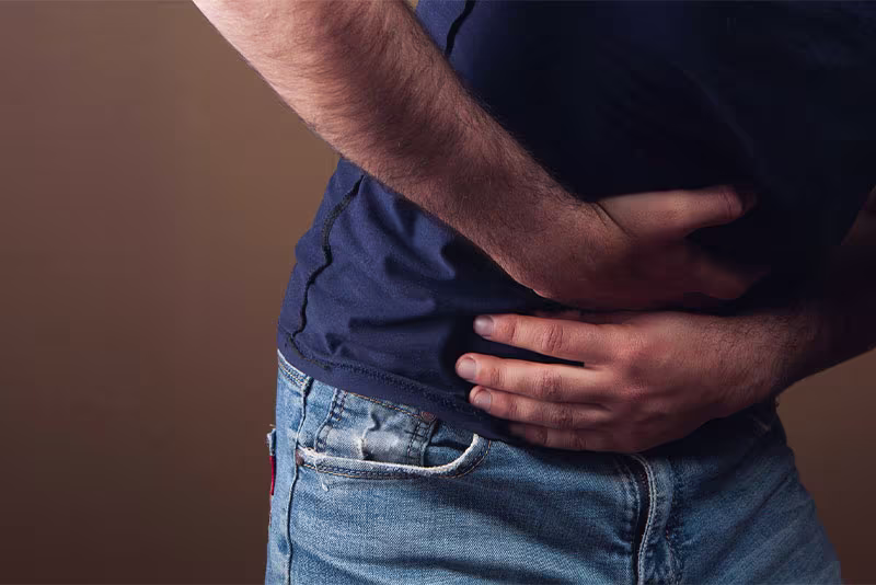 Person wearing a navy shirt and jeans clutching their midsection with both hands, indicating stomach or abdominal discomfort.