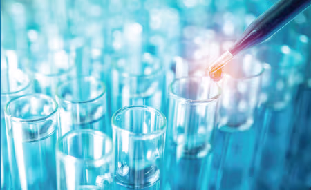 Pipette dispensing a drop into a row of clear test tubes in a blue-toned laboratory environment.