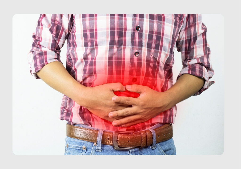 Person in a plaid shirt and jeans clutching their stomach, with a red glow over the midsection indicating stomach pain.