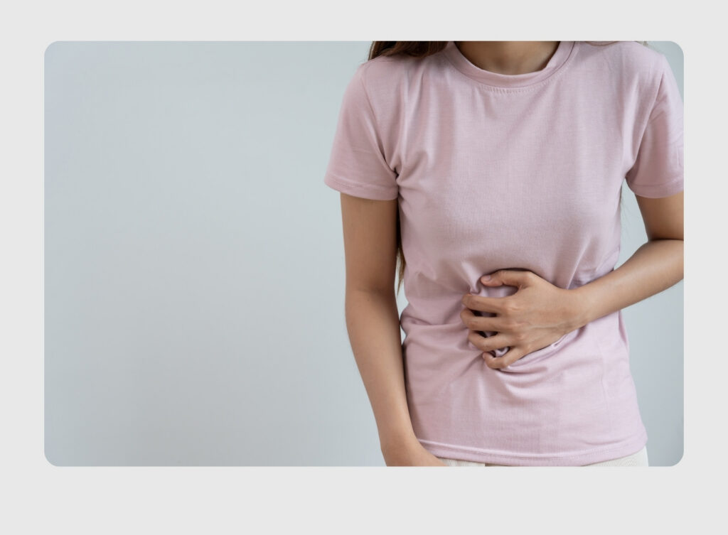 Person in a pink T-shirt clutching their stomach, suggesting abdominal pain or discomfort.