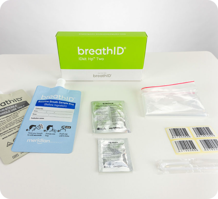 BreathID kit on a white table: green-and-white box labeled breathID, blue instruction card, foil sachets, clear bags with labels, and barcode sheets/items.