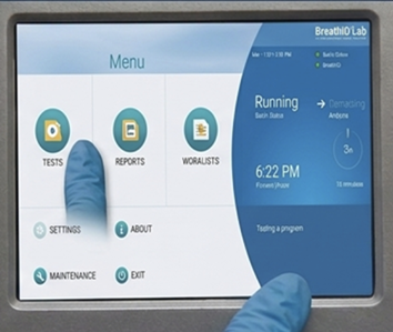 Touchscreen interface showing a Menu with icons for Tests, Reports, and World Lists; two gloved fingers touch the screen.