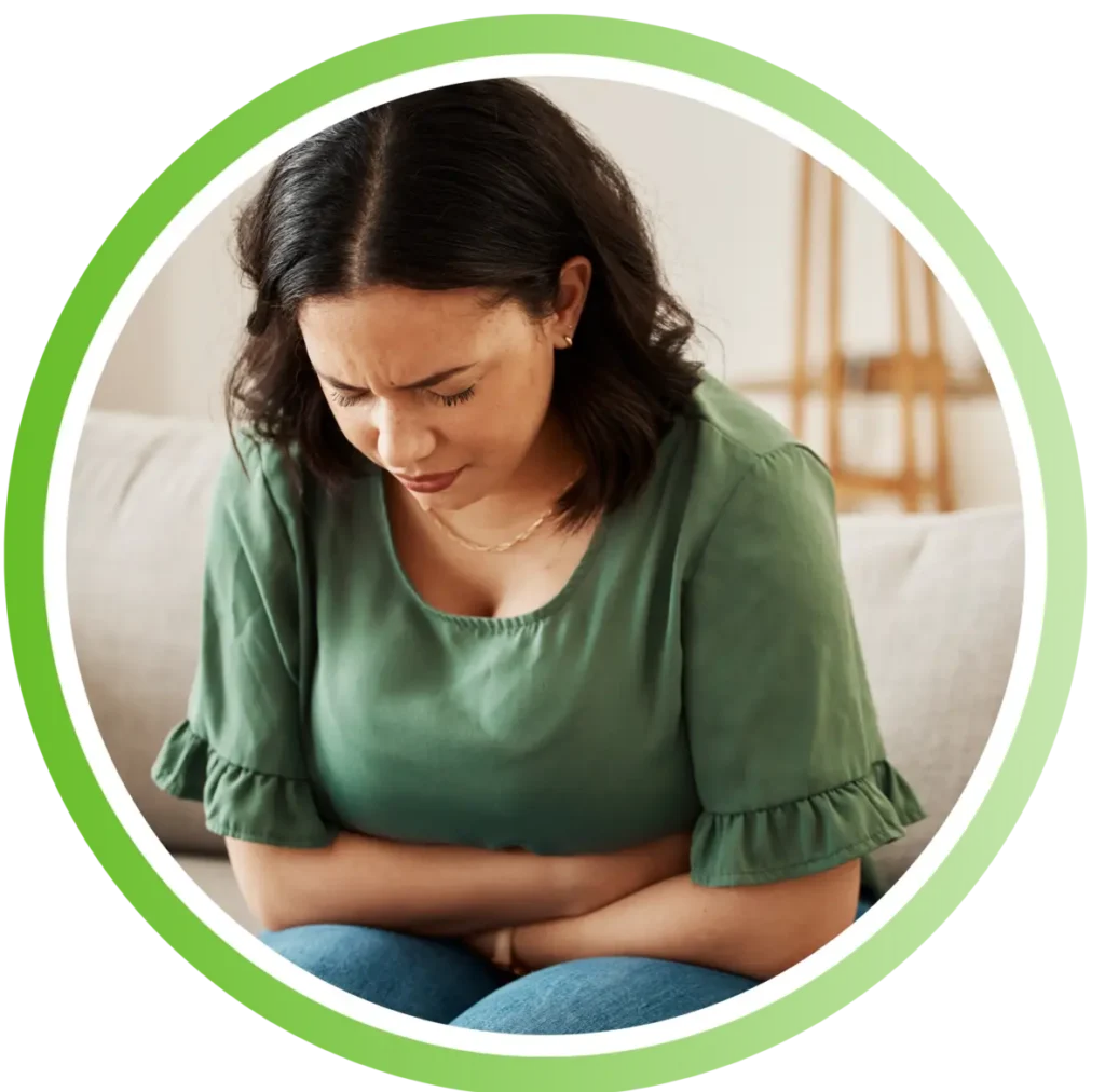 Woman sitting on a couch, clutching her stomach and grimacing in pain.