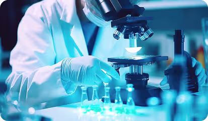 Scientist wearing gloves and a lab coat uses a compound microscope in a laboratory.