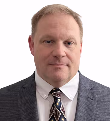Headshot of a middle-aged man in a gray suit, white shirt, and patterned tie, facing the camera with a neutral expression against a white background.