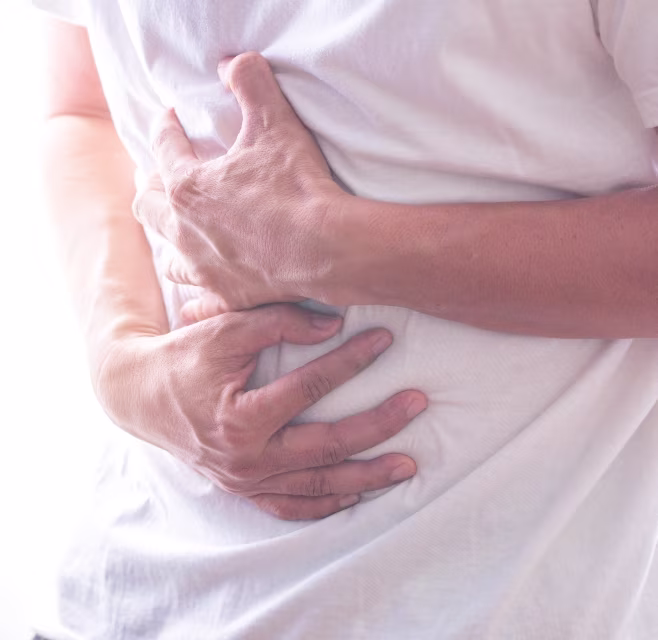 Person holding their abdomen with both hands, conveying stomach pain or discomfort while wearing a white shirt